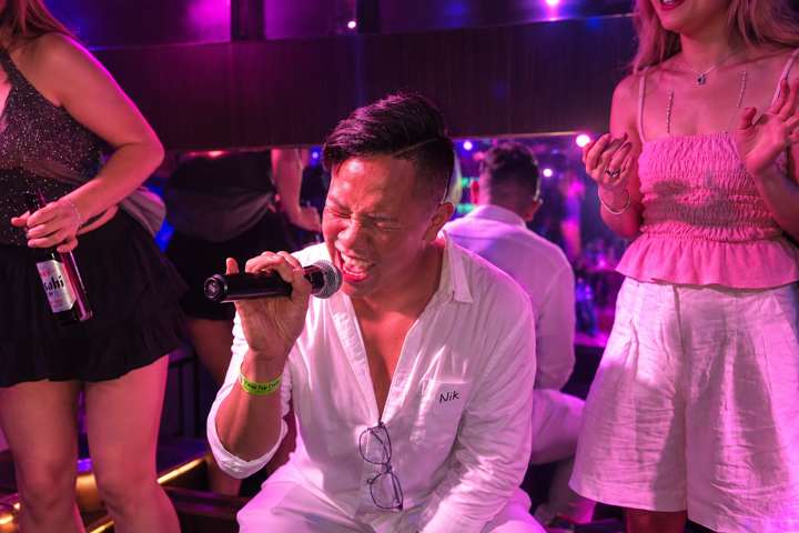 A guest singing into a microphone under pink lights at a Tokyo Pub Crawl event